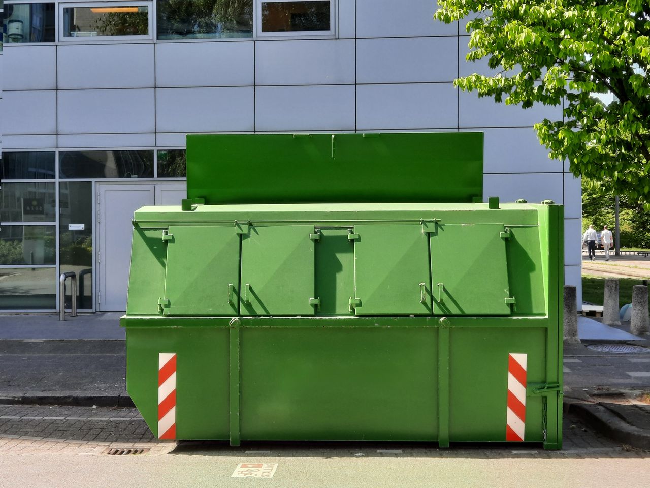 A green dumpster is placed outside an urban building in Den Haag.
